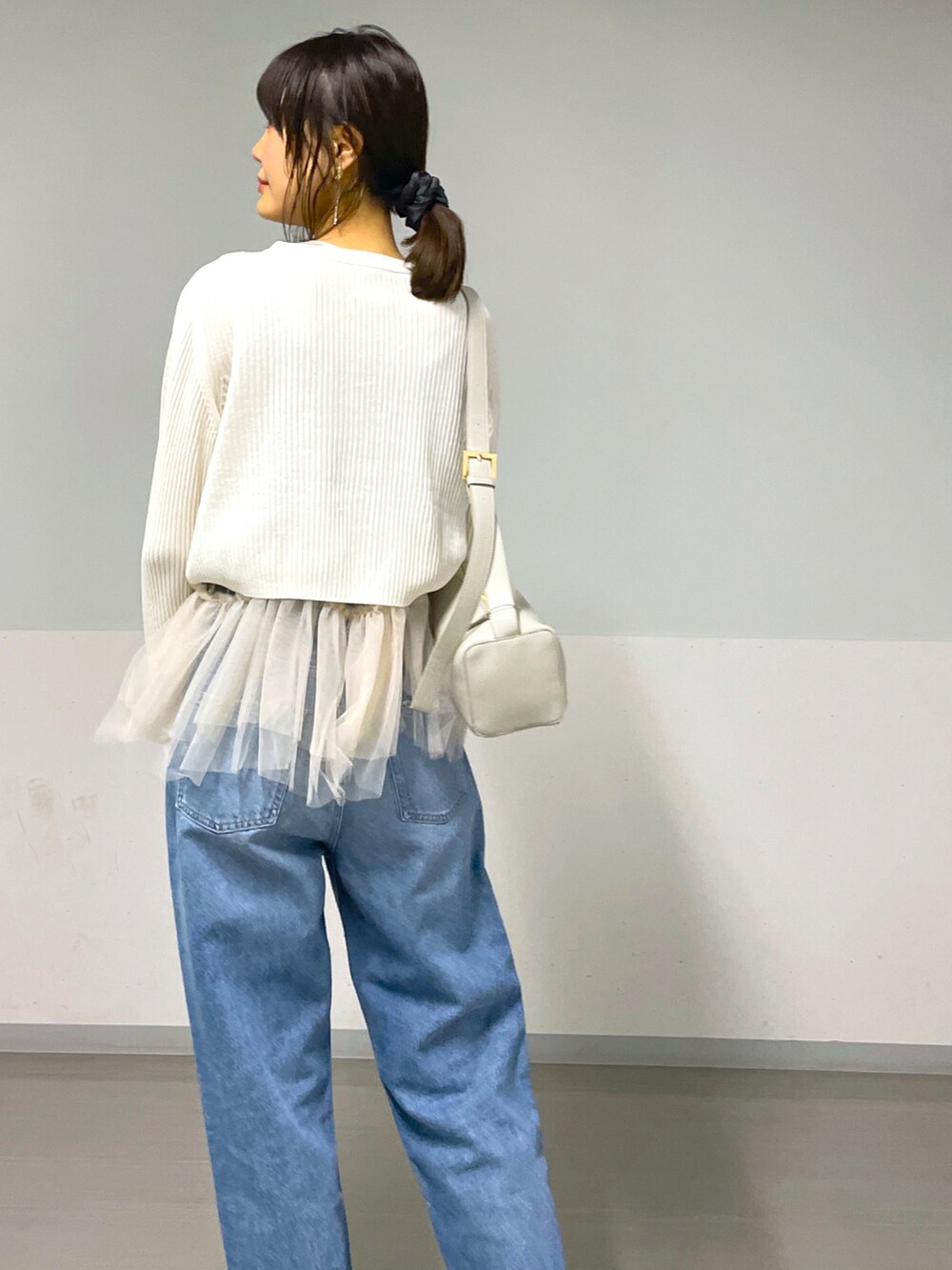 グレー系のショルダーバッグ、ホワイト系のベスト、ブルー系のデニムパンツを着用したレディースの秋コーディネートの2枚目の写真