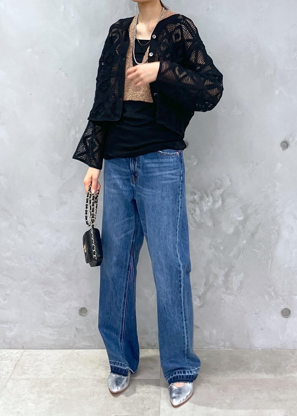 ブラック系のショルダーバッグ、ブルー系のデニムパンツ、ゴールド系のベストを着用したレディースの春コーディネートの7枚目の写真