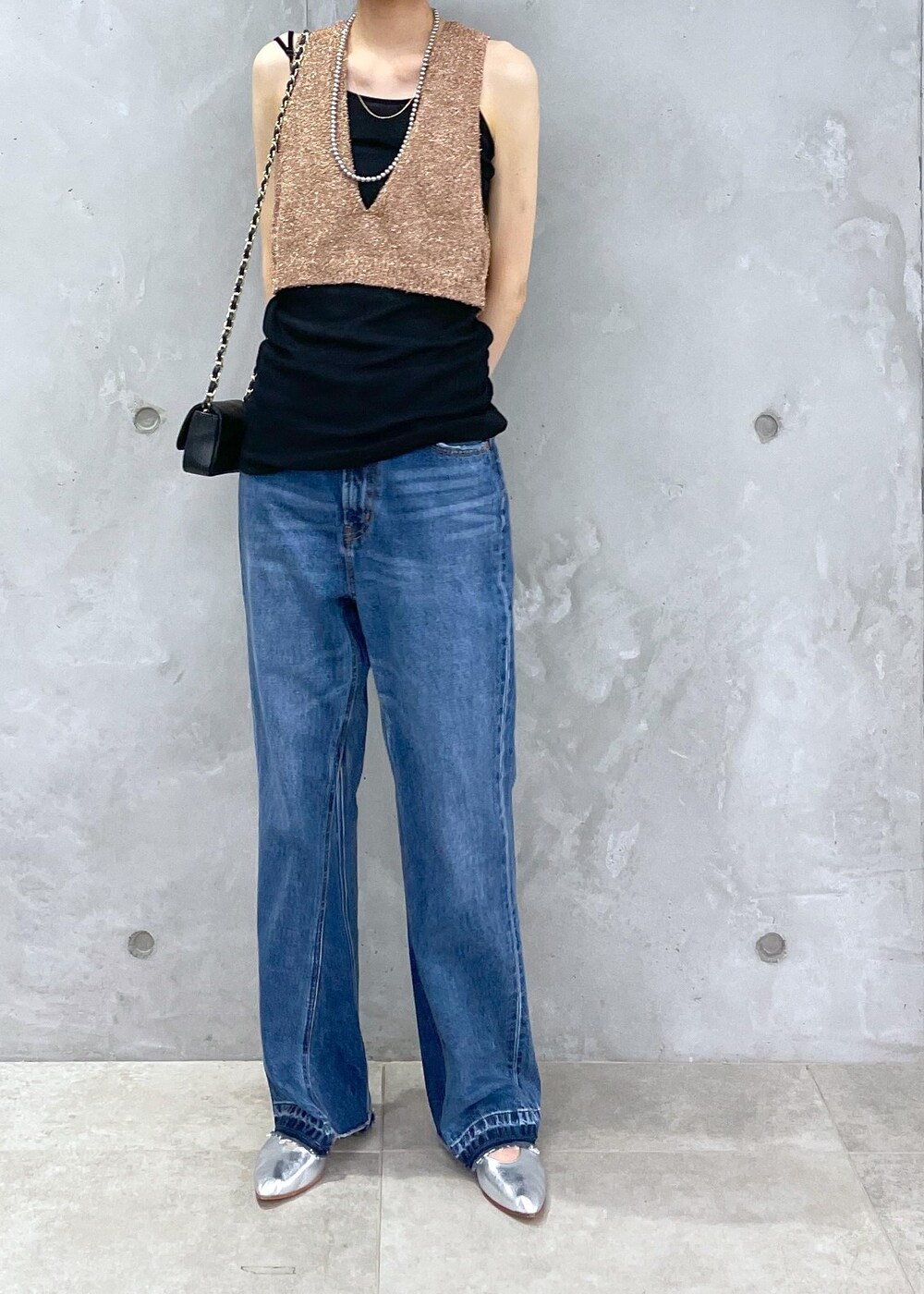 ブラック系のショルダーバッグ、ブルー系のデニムパンツ、ゴールド系のベストを着用したレディースの春コーディネートの9枚目の写真