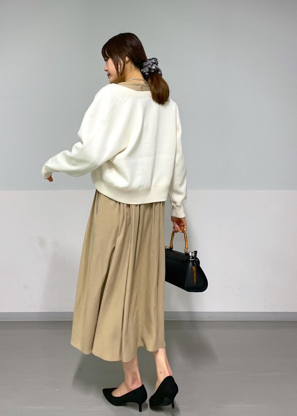 ブラック系のショルダーバッグ、ベージュ系のワンピース、ホワイト系のカーディガン/ボレロを着用したレディースの春コーディネートの6枚目の写真