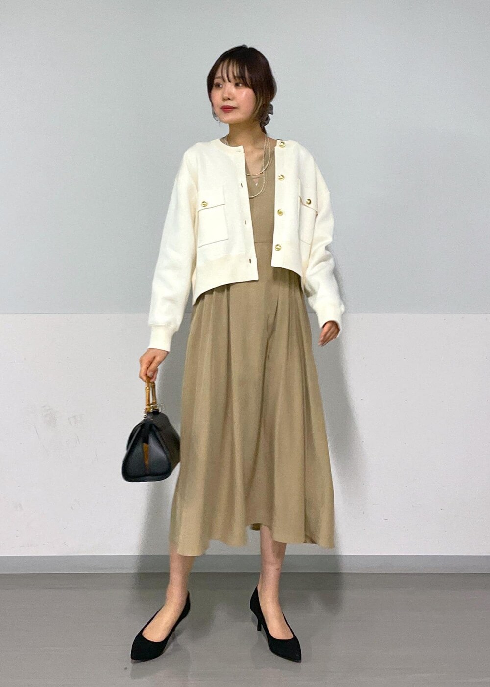 ブラック系のショルダーバッグ、ベージュ系のワンピース、ホワイト系のカーディガン/ボレロを着用したレディースの春コーディネートの7枚目の写真