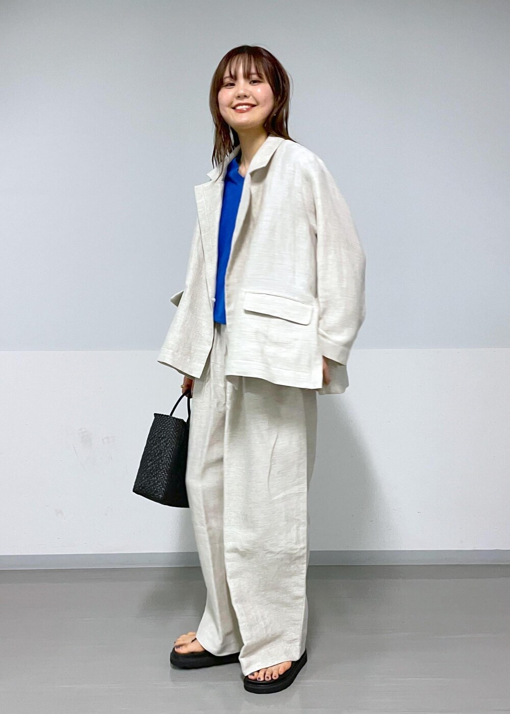 ブラック系のかごバッグ、ホワイト系のスラックス、ホワイト系のテーラードジャケットを着用したレディースの春コーディネートの3枚目の写真