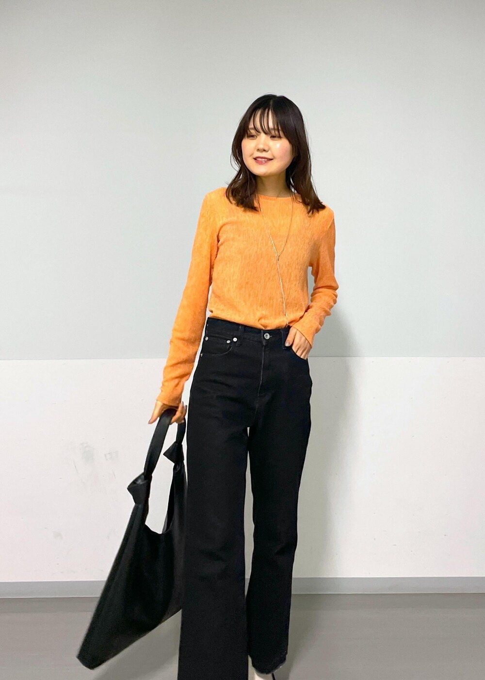 ブラック系のトートバッグ、グレー系のデニムパンツ、オレンジ系のTシャツ/カットソーを着用したレディースの冬コーディネートの7枚目の写真