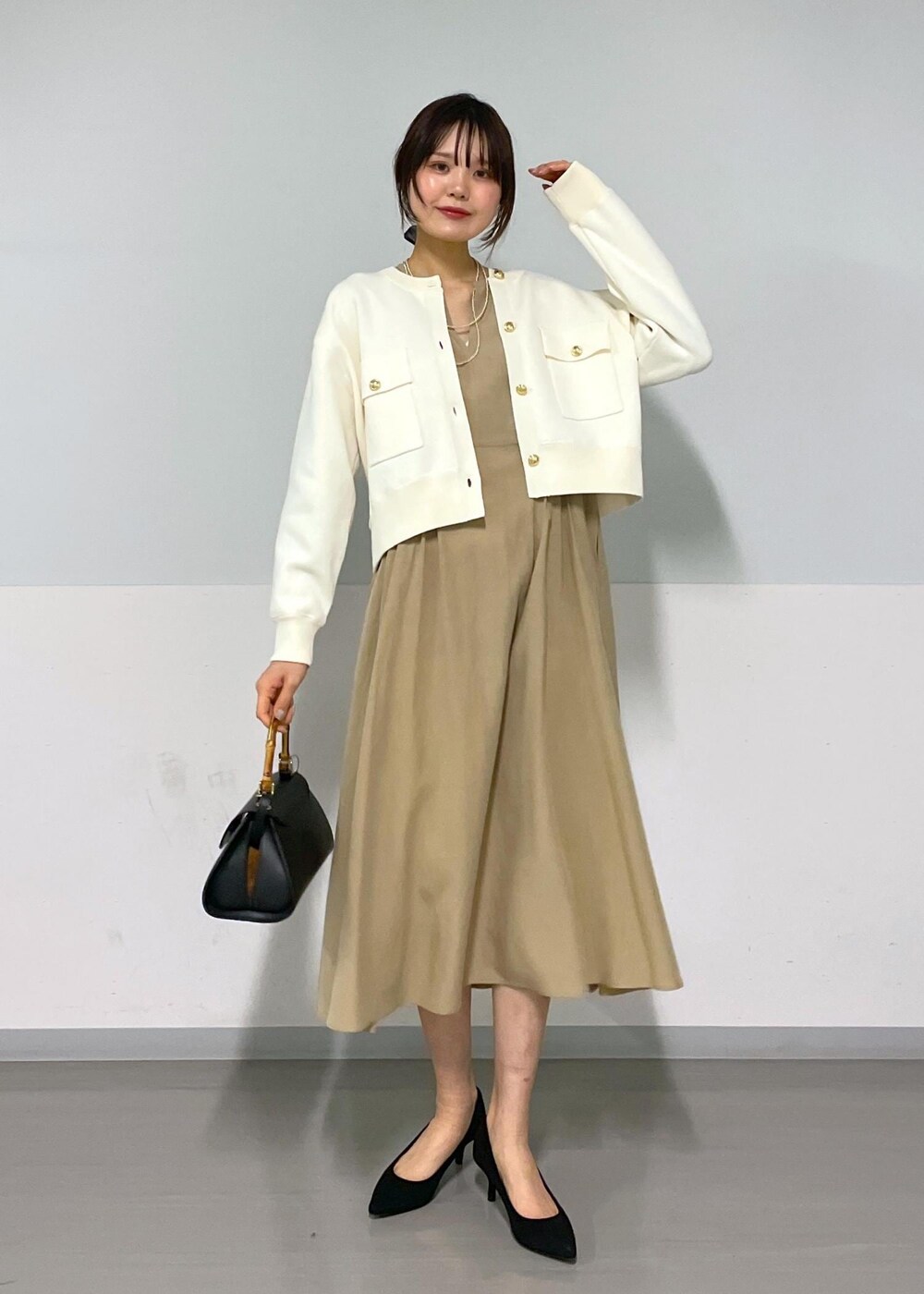 ブラック系のショルダーバッグ、ベージュ系のワンピース、ホワイト系のカーディガン/ボレロを着用したレディースの春コーディネートの2枚目の写真