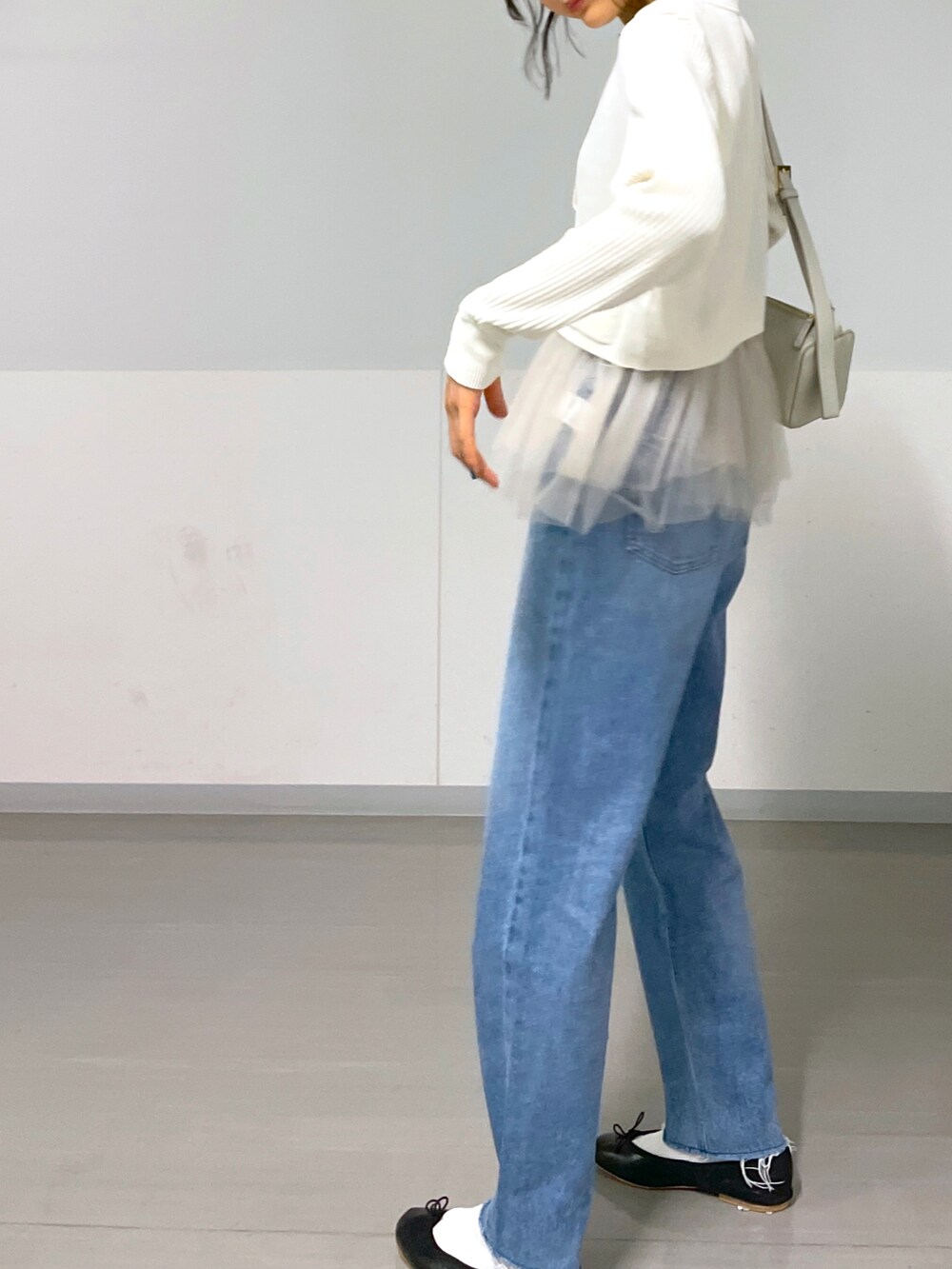 グレー系のショルダーバッグ、ホワイト系のベスト、ブルー系のデニムパンツを着用したレディースの秋コーディネートの4枚目の写真