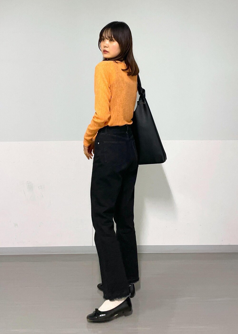 ブラック系のトートバッグ、グレー系のデニムパンツ、オレンジ系のTシャツ/カットソーを着用したレディースの冬コーディネートの6枚目の写真