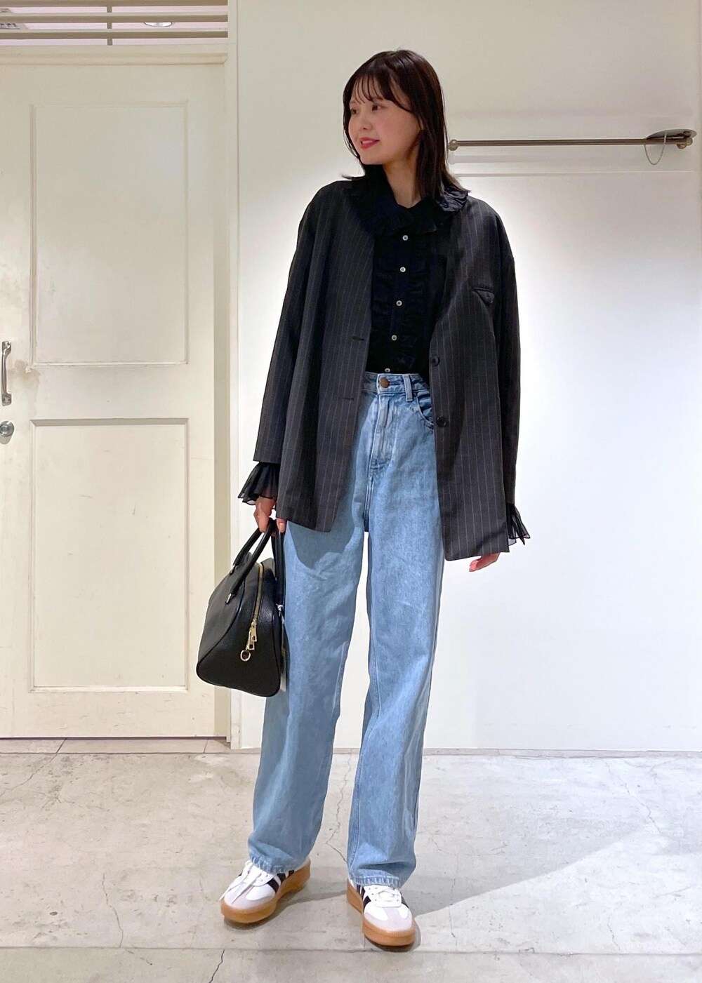 グレー系のノーカラージャケット、ブルー系のデニムパンツ、ブラック系のボストンバッグを着用したレディースの夏コーディネートの2枚目の写真