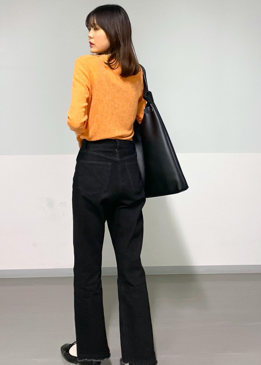 ブラック系のトートバッグ、グレー系のデニムパンツ、オレンジ系のTシャツ/カットソーを着用したレディースの冬コーディネートの3枚目の写真