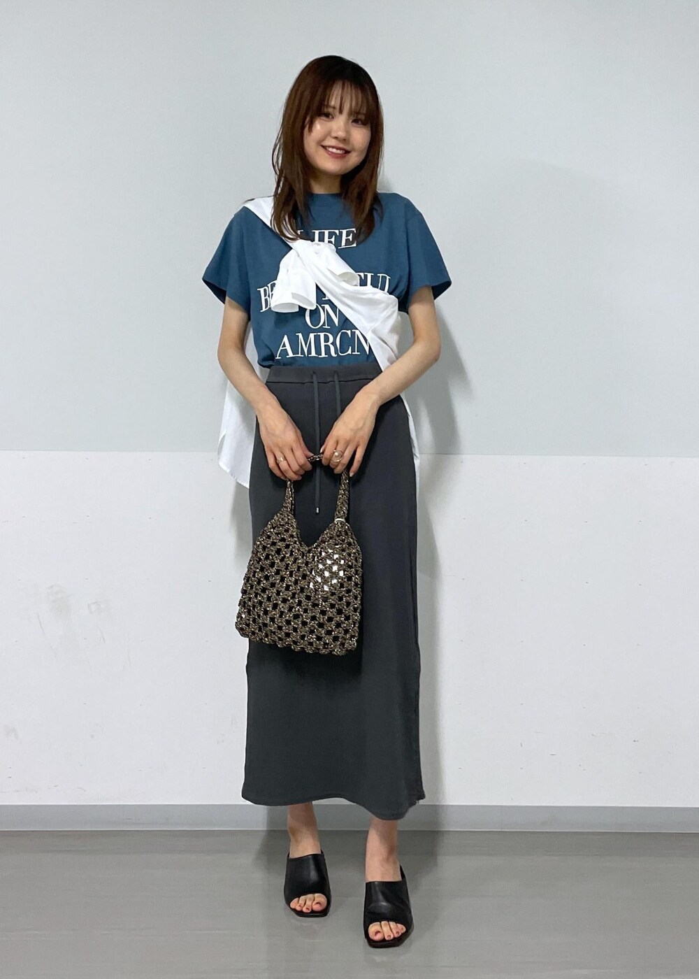 ブルー系のTシャツ/カットソー、ブラック系のハンドバッグ、グレー系のスカートを着用したレディースの夏コーディネートの2枚目の写真