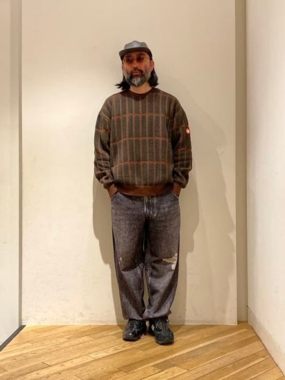 ブラウン系のニット/セーター、ブラック系のキャップ、ベージュ系のサングラスを着用したメンズの春コーディネートの2枚目の写真