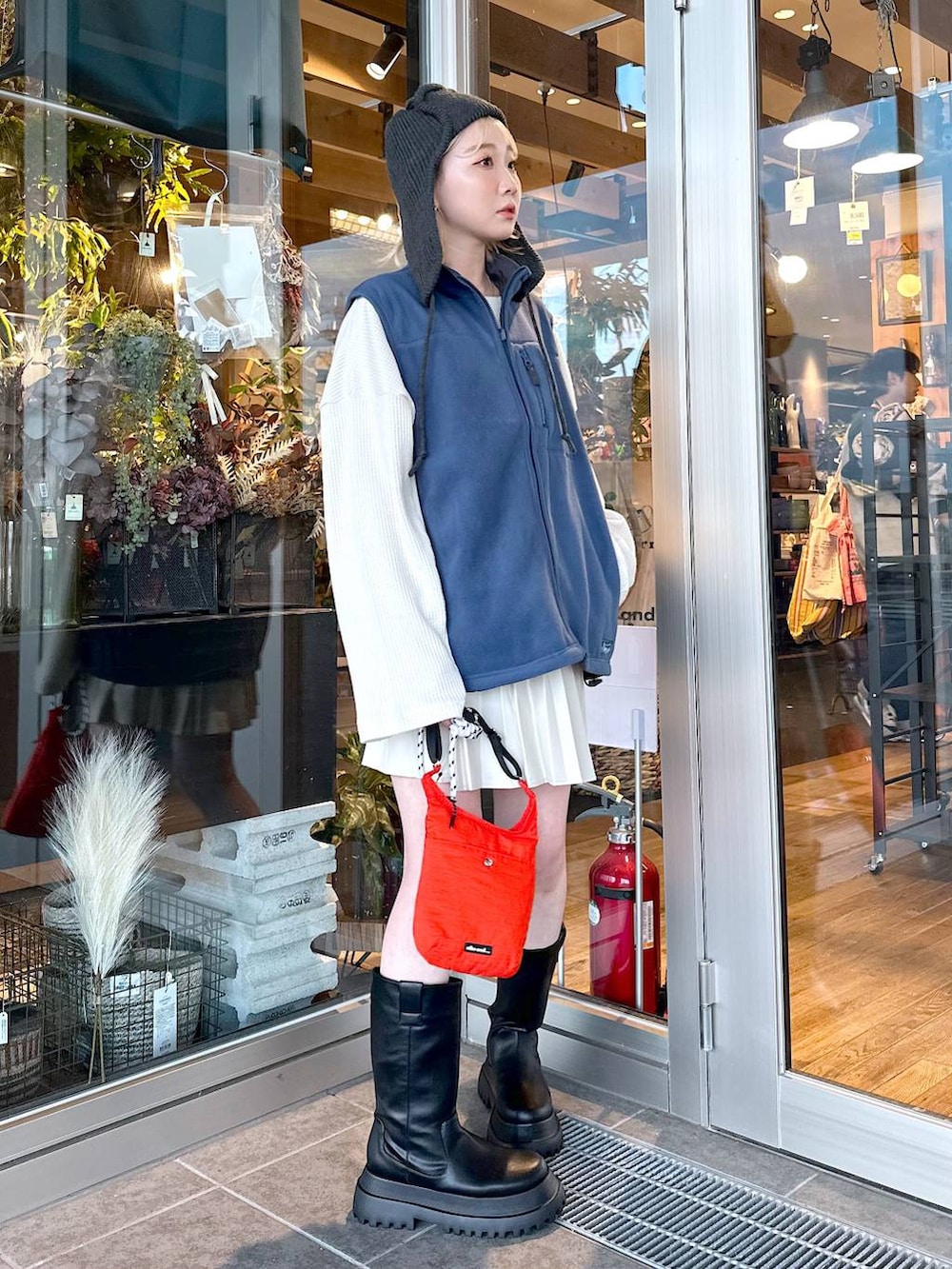 レッド系のショルダーバッグ、ブルー系のベスト、ブラック系のブーツを着用したレディースの秋コーディネートの3枚目の写真