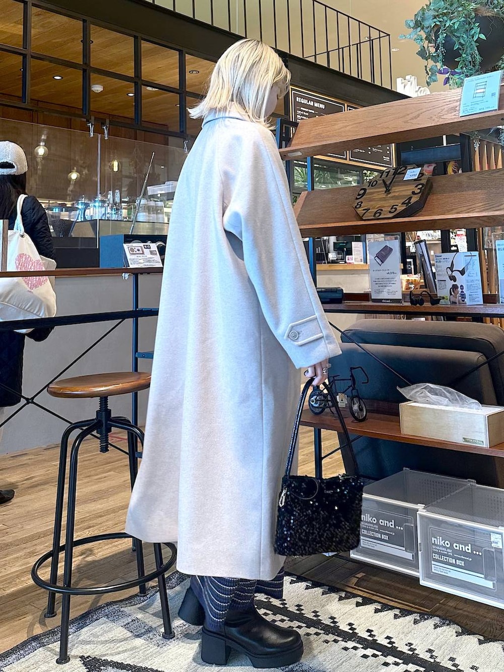 ベージュ系のステンカラーコート、ブラック系のブーツ、ブルー系のスカートを着用したレディースの冬コーディネートの2枚目の写真