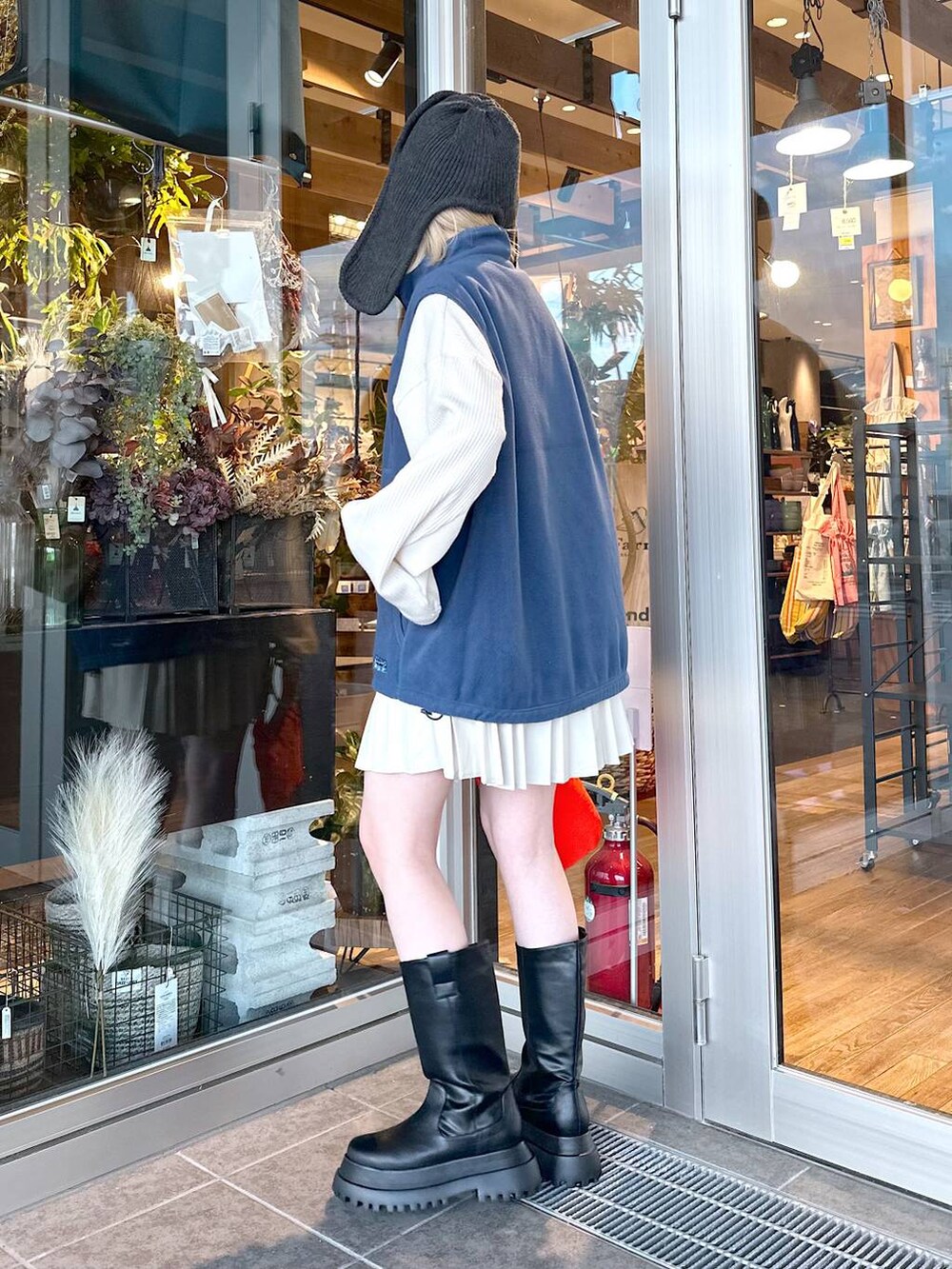 レッド系のショルダーバッグ、ブルー系のベスト、ブラック系のブーツを着用したレディースの秋コーディネートの2枚目の写真