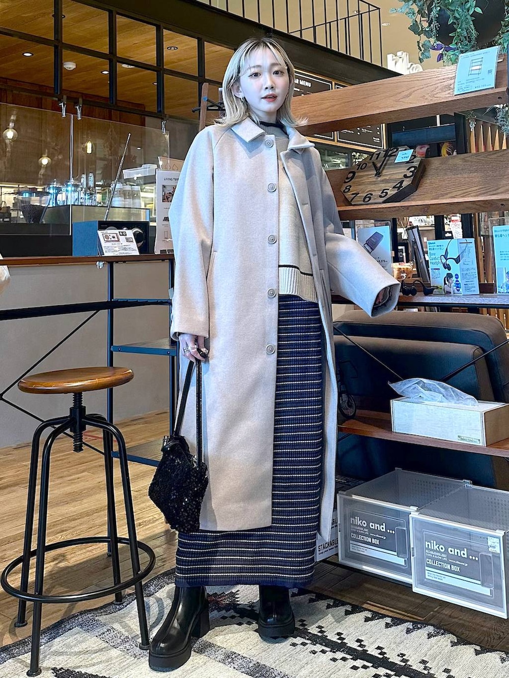 ベージュ系のステンカラーコート、ブラック系のブーツ、ブルー系のスカートを着用したレディースの冬コーディネートの3枚目の写真