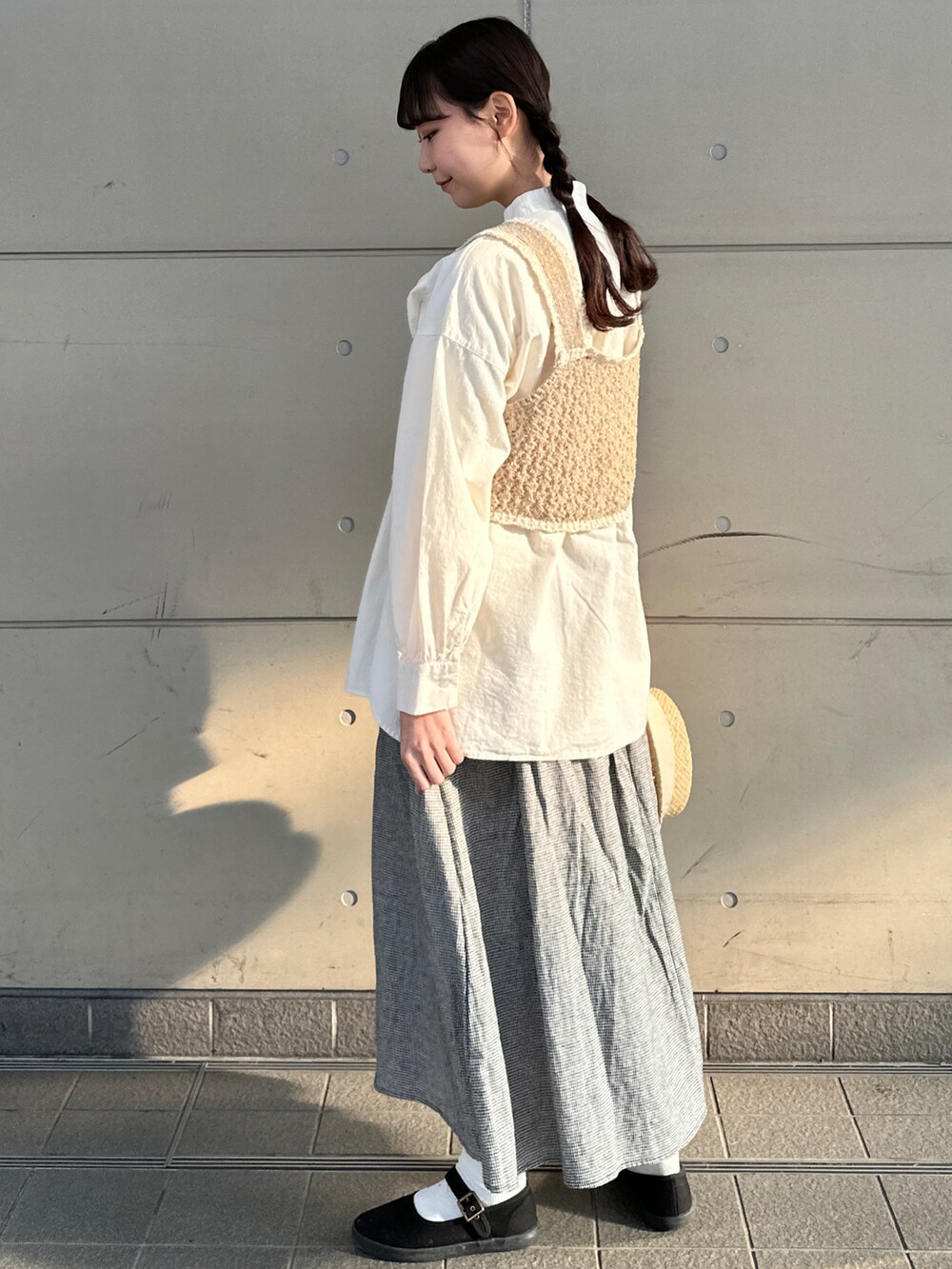 ホワイト系のチュニック、ブラウン系のベスト、グレー系のスカートを着用したレディースの春コーディネートの2枚目の写真