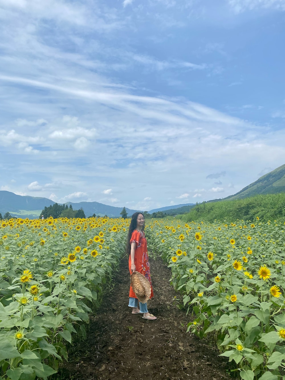 レッド系のワンピース、ブルー系のデニムパンツ、ホワイト系のサンダルを着用したレディースの夏コーディネートの2枚目の写真