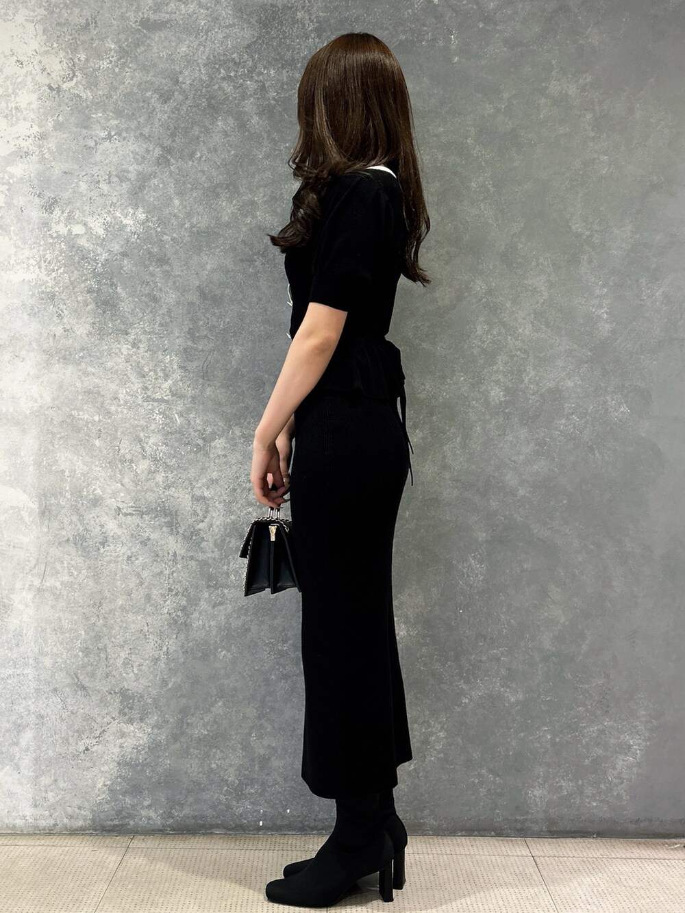 ブラック系のスカート、ブラック系のニット/セーター、ブラック系のハンドバッグを着用したレディースの春コーディネートの2枚目の写真