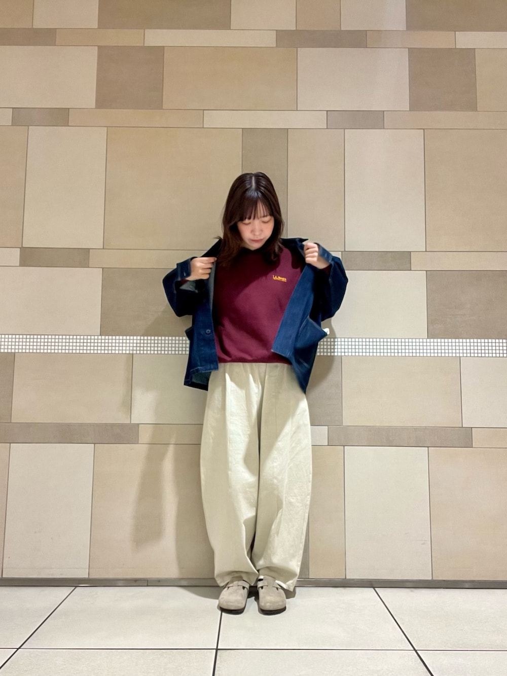 レッド系のスウェット、ブルー系のカバーオール、ベージュ系のサンダルを着用したレディースの秋コーディネートの2枚目の写真