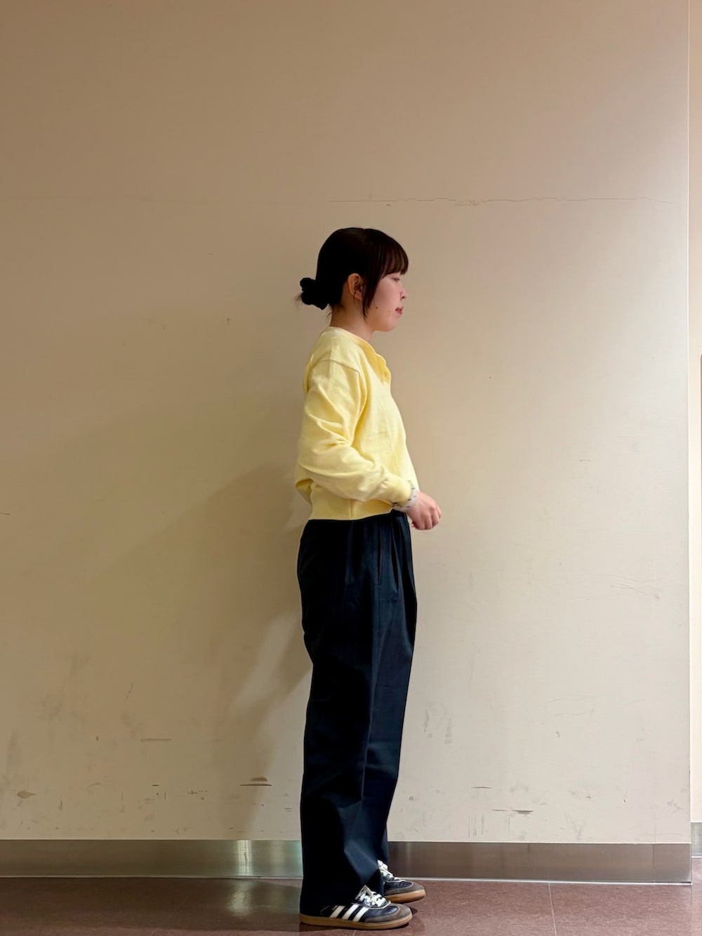 イエロー系のニット/セーター、グレー系のスラックス、ホワイト系のTシャツ/カットソーを着用したレディースの冬コーディネートの2枚目の写真