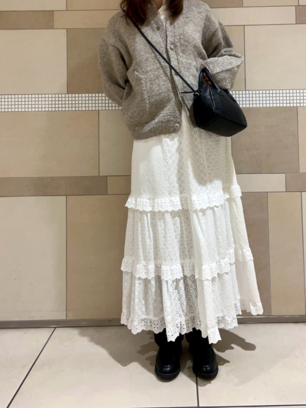 グレー系のカーディガン/ボレロ、ブラック系のハンドバッグ、ホワイト系のスカートを着用したレディースの秋コーディネートの2枚目の写真