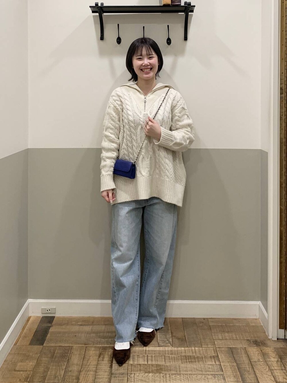 ブルー系のショルダーバッグ、ホワイト系のニット/セーター、ブルー系のデニムパンツを着用したレディースの冬コーディネートの2枚目の写真