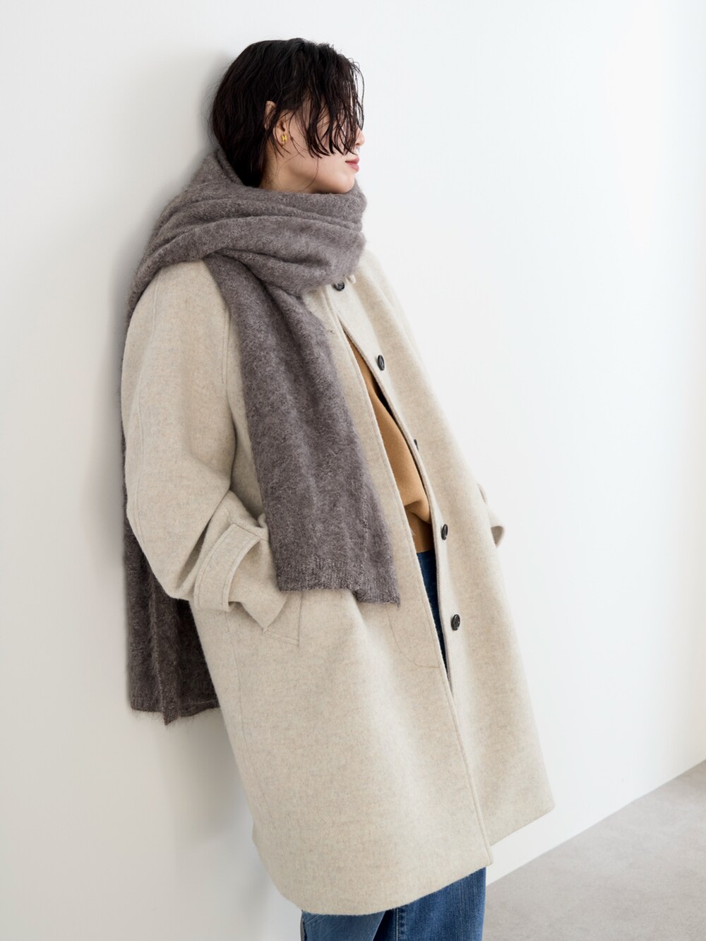 ベージュ系のステンカラーコート、イエロー系のニット/セーター、ブルー系のデニムパンツを着用したレディースの冬コーディネートの3枚目の写真