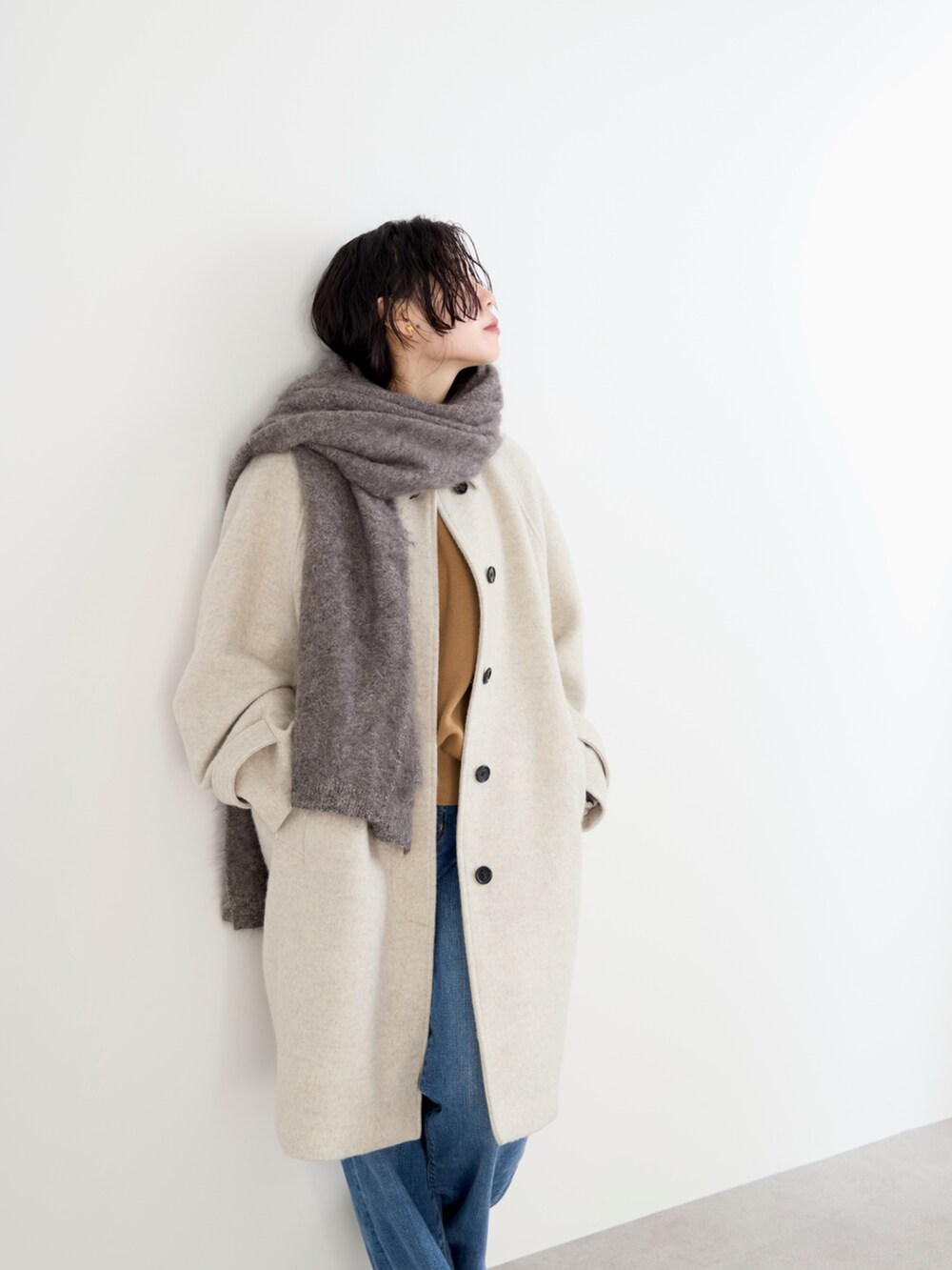ベージュ系のステンカラーコート、イエロー系のニット/セーター、ブルー系のデニムパンツを着用したレディースの冬コーディネートの4枚目の写真