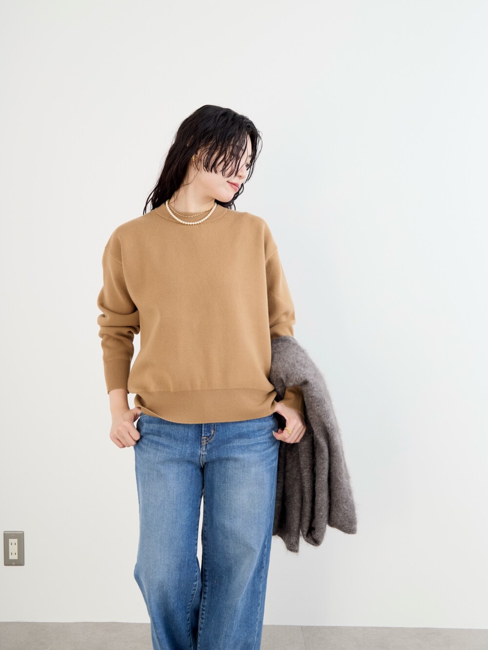 ベージュ系のステンカラーコート、イエロー系のニット/セーター、ブルー系のデニムパンツを着用したレディースの冬コーディネートの9枚目の写真
