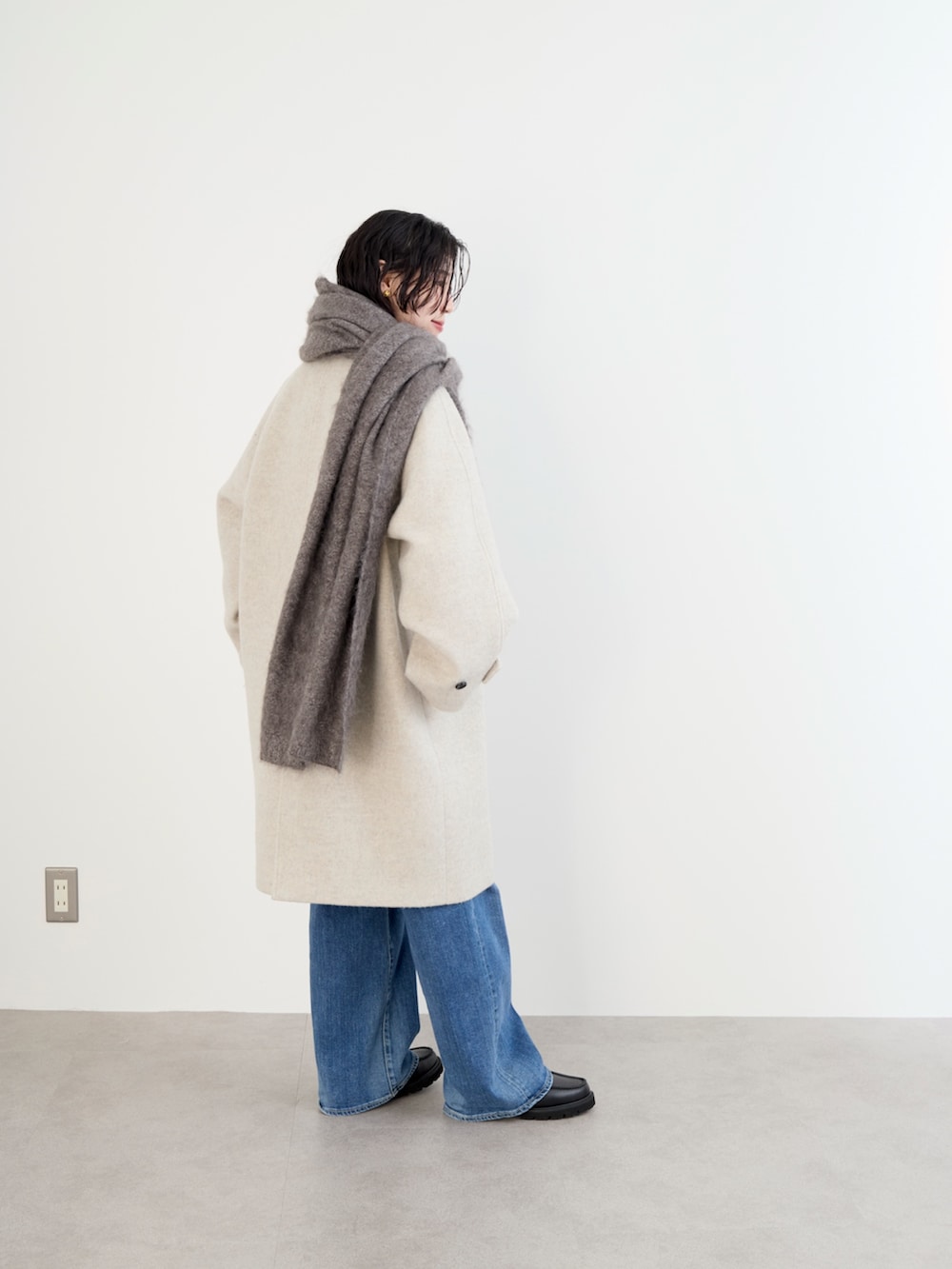 ベージュ系のステンカラーコート、イエロー系のニット/セーター、ブルー系のデニムパンツを着用したレディースの冬コーディネートの5枚目の写真