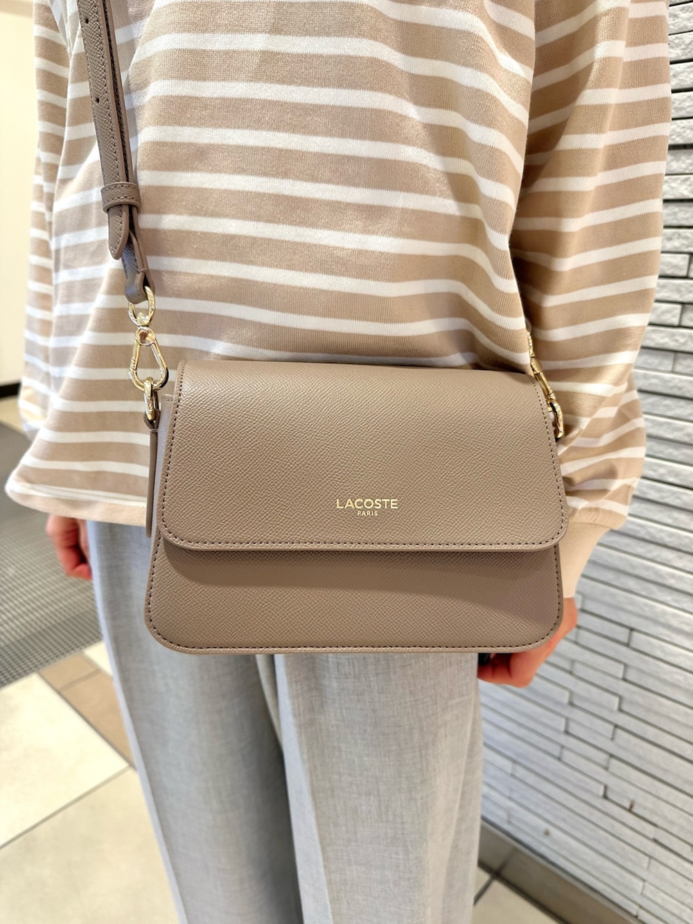 ベージュ系のトップス、ベージュ系のバッグ、グレー系のパンツを着用したレディースの冬コーディネートの4枚目の写真