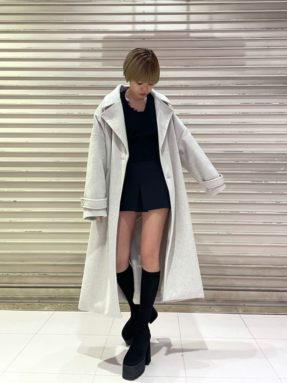 ホワイト系のチェスターコート、ブラック系のスカート、ブラック系のブーツを着用したレディースの冬コーディネートの2枚目の写真