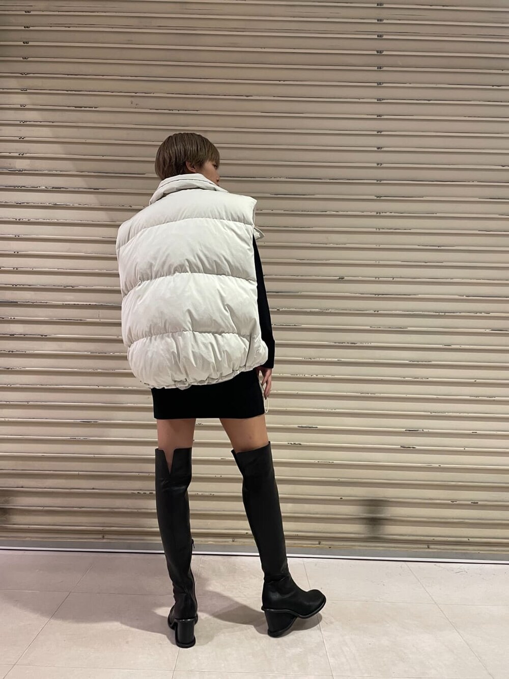 ホワイト系のダウンベスト、ブラック系のブーツ、ブラック系のワンピースを着用したレディースの秋コーディネートの5枚目の写真