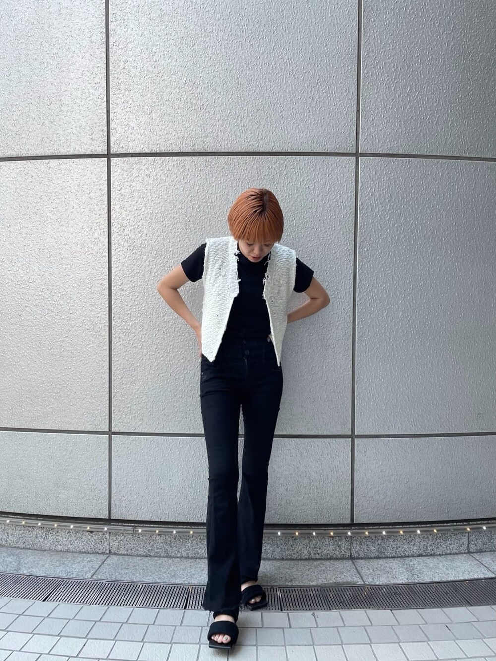 ブラック系のデニムパンツ、ホワイト系のベスト、ブラック系のサンダルを着用したレディースの夏コーディネートの2枚目の写真