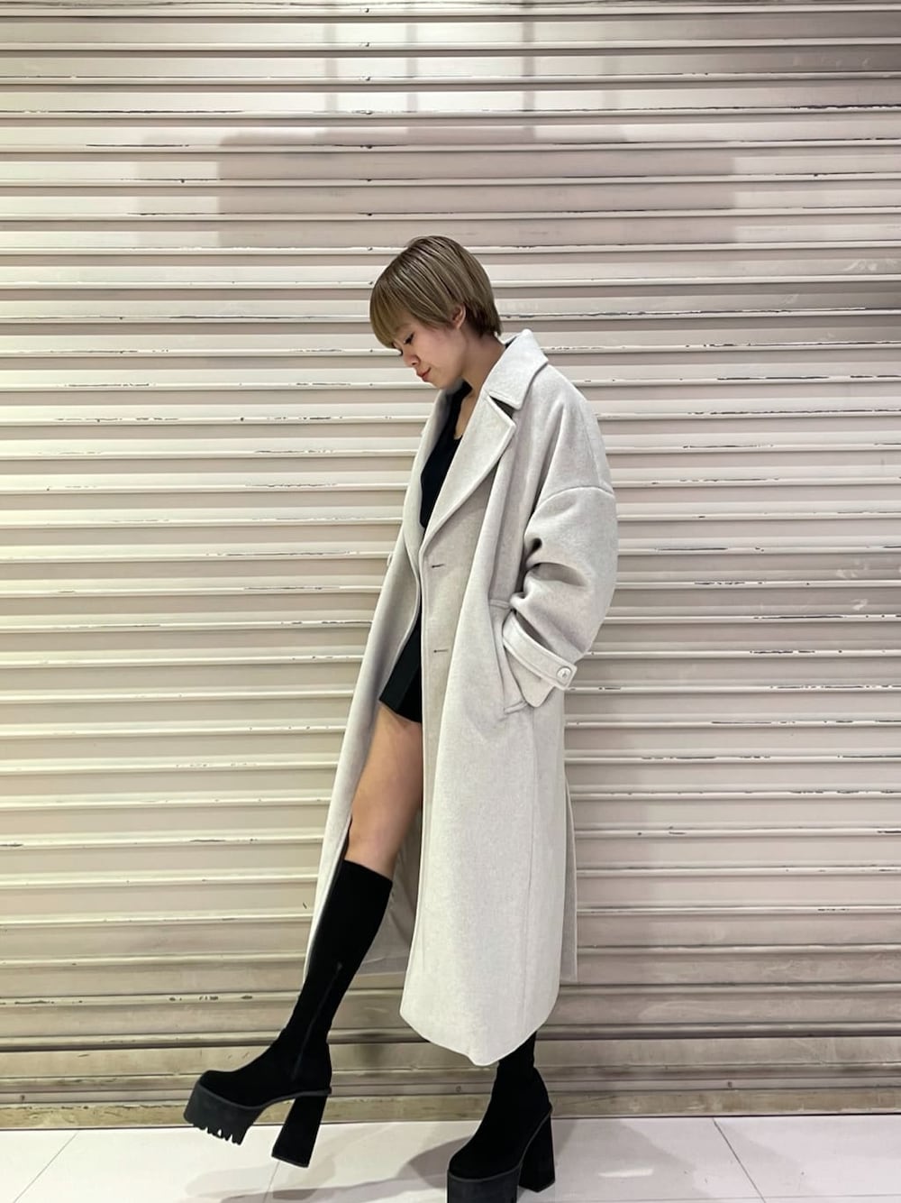 ホワイト系のチェスターコート、ブラック系のスカート、ブラック系のブーツを着用したレディースの冬コーディネートの3枚目の写真