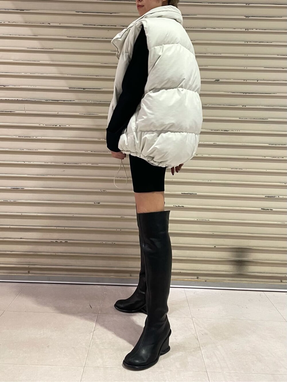 ホワイト系のダウンベスト、ブラック系のブーツ、ブラック系のワンピースを着用したレディースの秋コーディネートの3枚目の写真