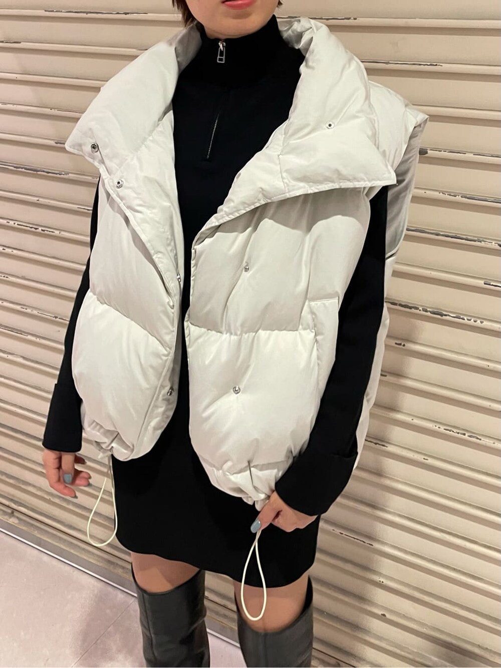 ホワイト系のダウンベスト、ブラック系のブーツ、ブラック系のワンピースを着用したレディースの秋コーディネートの6枚目の写真