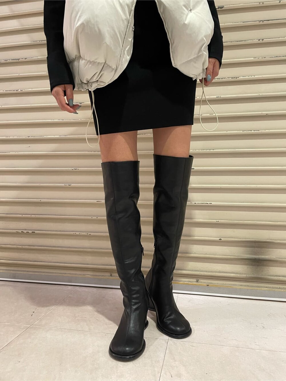 ホワイト系のダウンベスト、ブラック系のブーツ、ブラック系のワンピースを着用したレディースの秋コーディネートの8枚目の写真