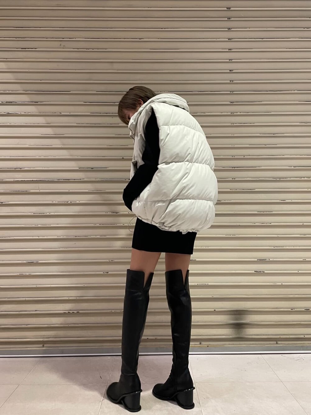 ホワイト系のダウンベスト、ブラック系のブーツ、ブラック系のワンピースを着用したレディースの秋コーディネートの4枚目の写真