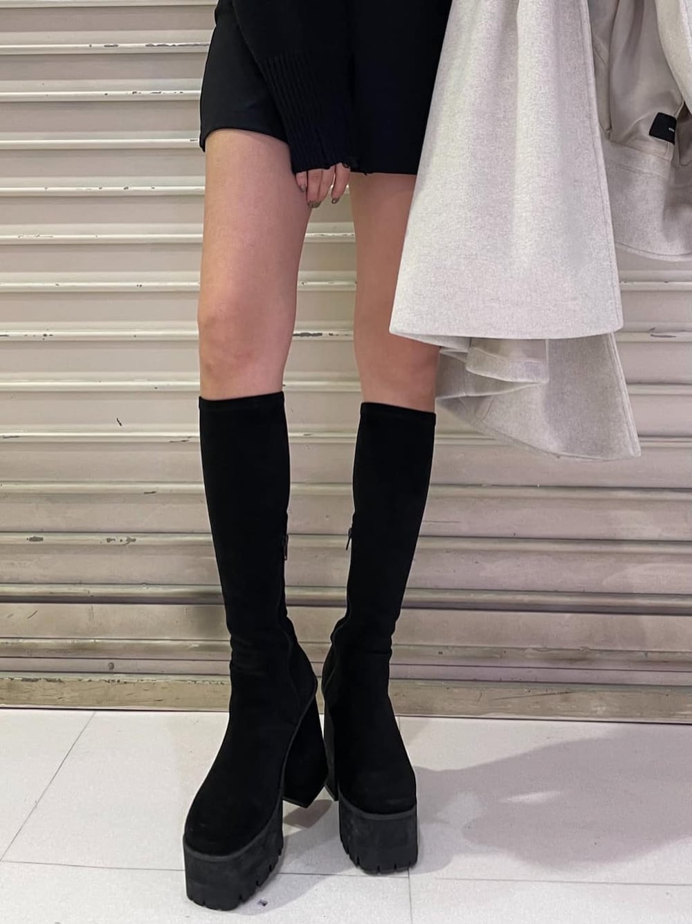 ホワイト系のチェスターコート、ブラック系のスカート、ブラック系のブーツを着用したレディースの冬コーディネートの7枚目の写真