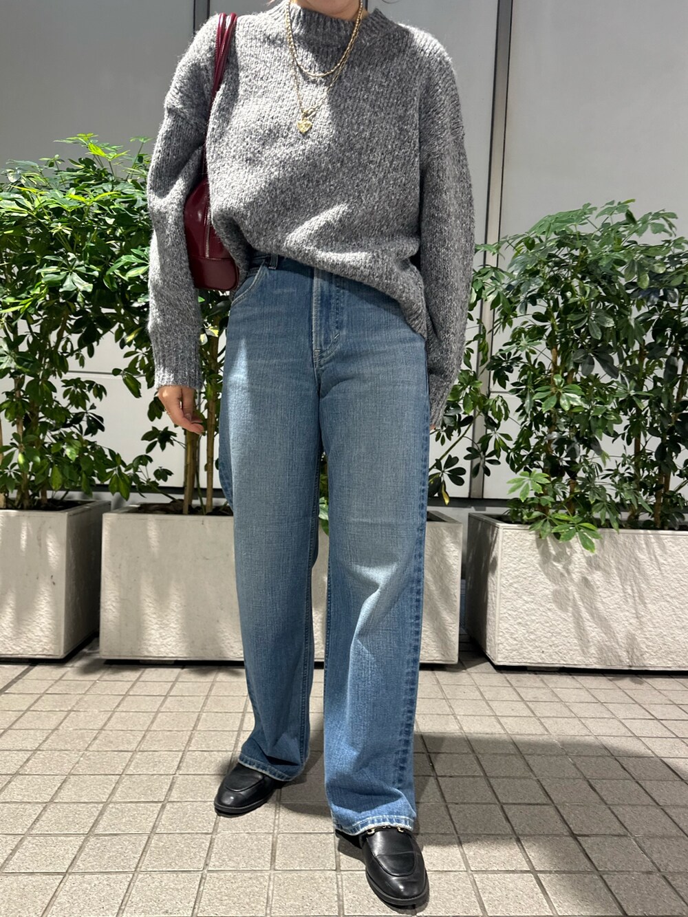 グレー系のニット/セーター、ブルー系のデニムパンツ、レッド系のハンドバッグを着用したレディースの秋コーディネートの5枚目の写真