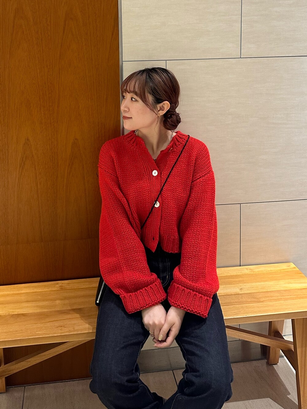 レッド系のカーディガン/ボレロ、ブルー系のデニムパンツ、ブラック系のショルダーバッグを着用したレディースの秋コーディネートの6枚目の写真