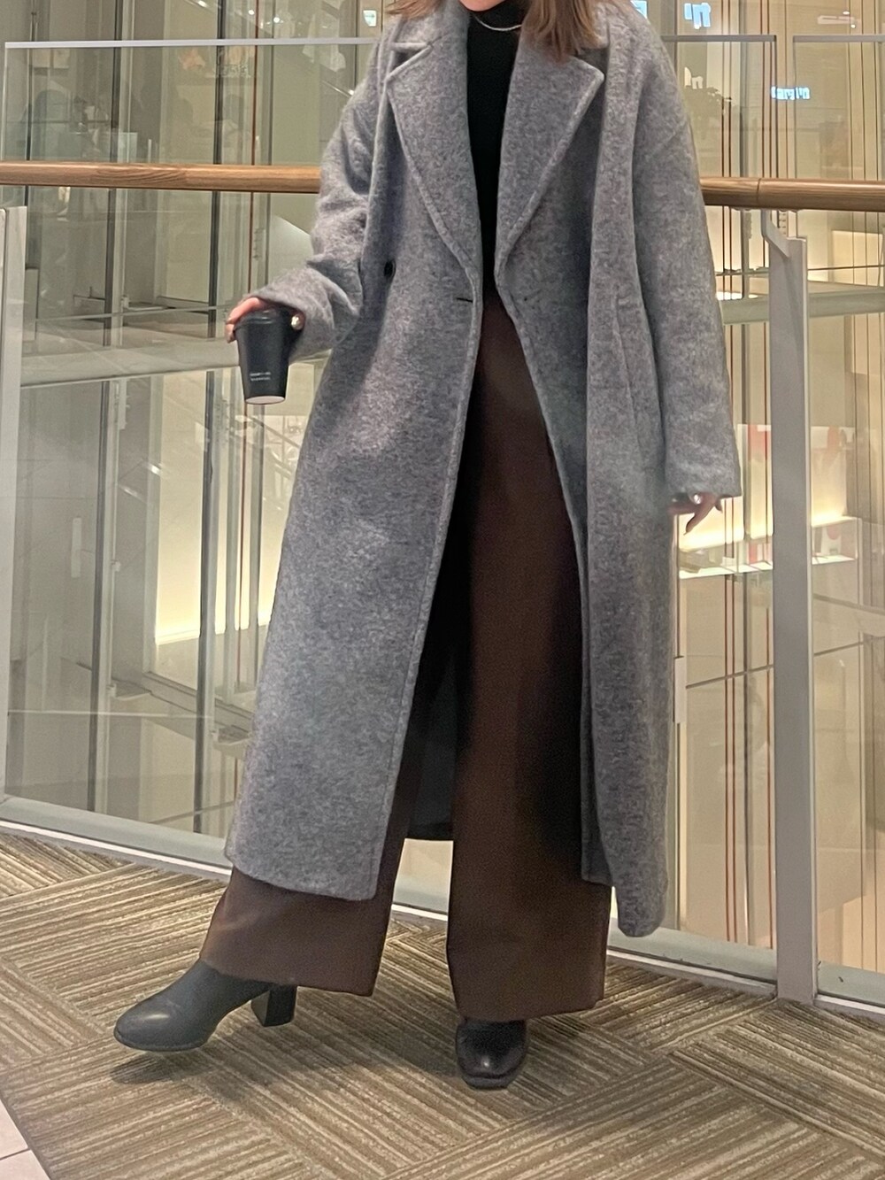 グレー系のチェスターコート、ブラウン系のその他パンツ、ブラック系のニット/セーターを着用したレディースの冬コーディネートの3枚目の写真