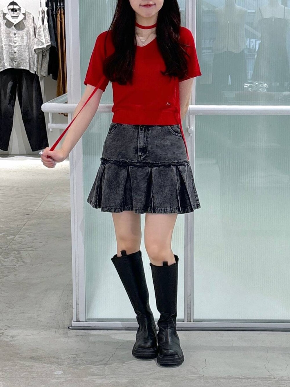 レッド系のニット/セーター、ブラック系のブーツ、ブラック系のデニムスカートを着用したレディースの夏コーディネートの2枚目の写真