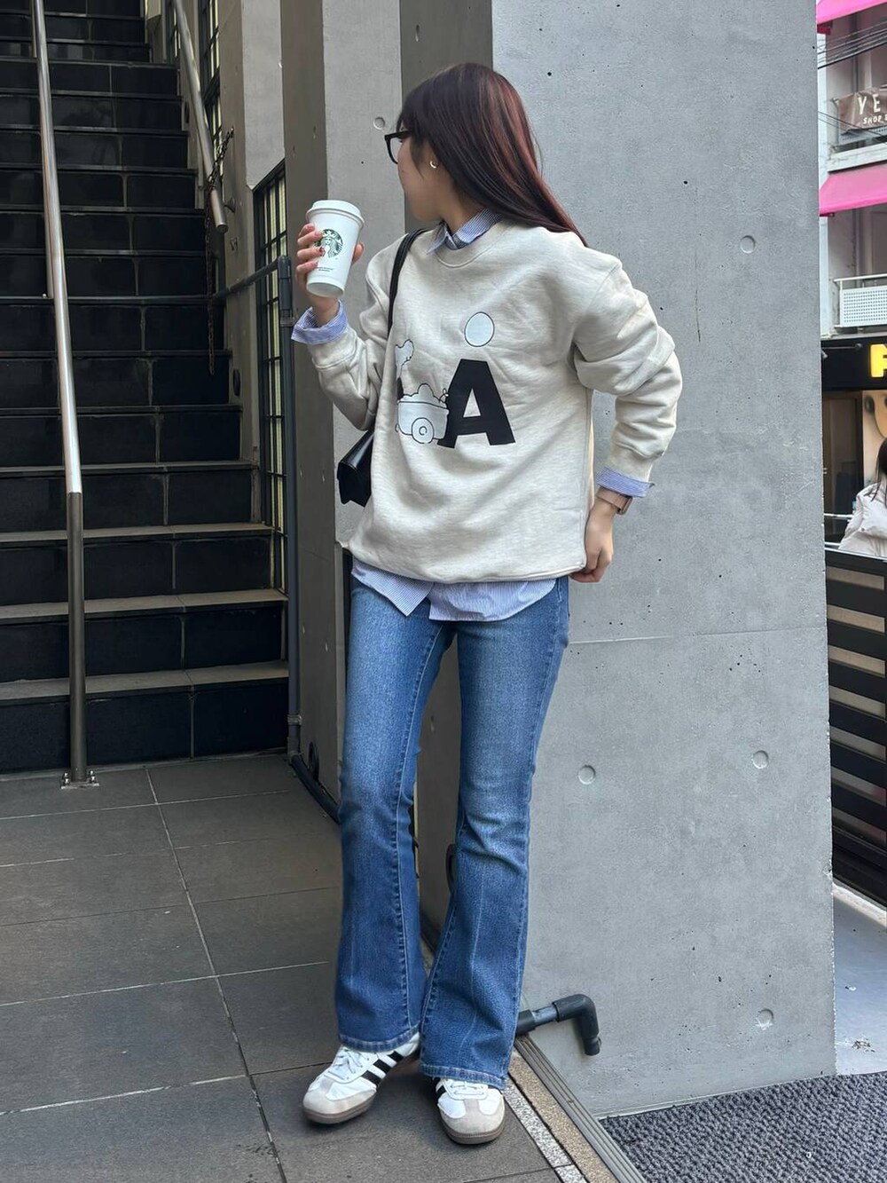 ブルー系のデニムパンツ、ブラック系のショルダーバッグ、ベージュ系のスウェットを着用したレディースの冬コーディネートの2枚目の写真
