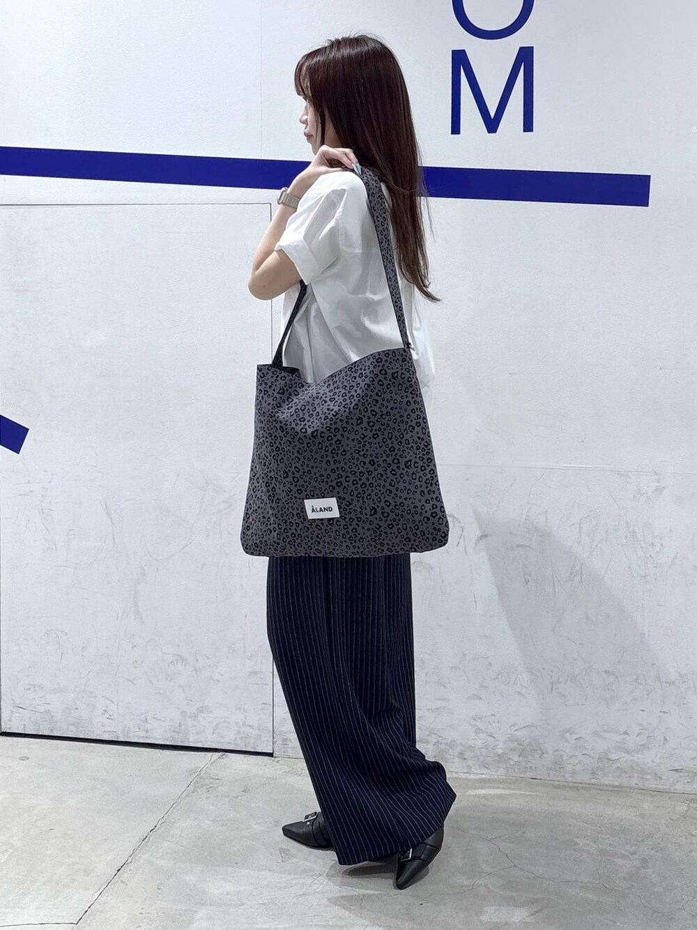グレー系のトートバッグ、ブラック系のパンプス、ブルー系のスラックスを着用したレディースの春コーディネートの3枚目の写真