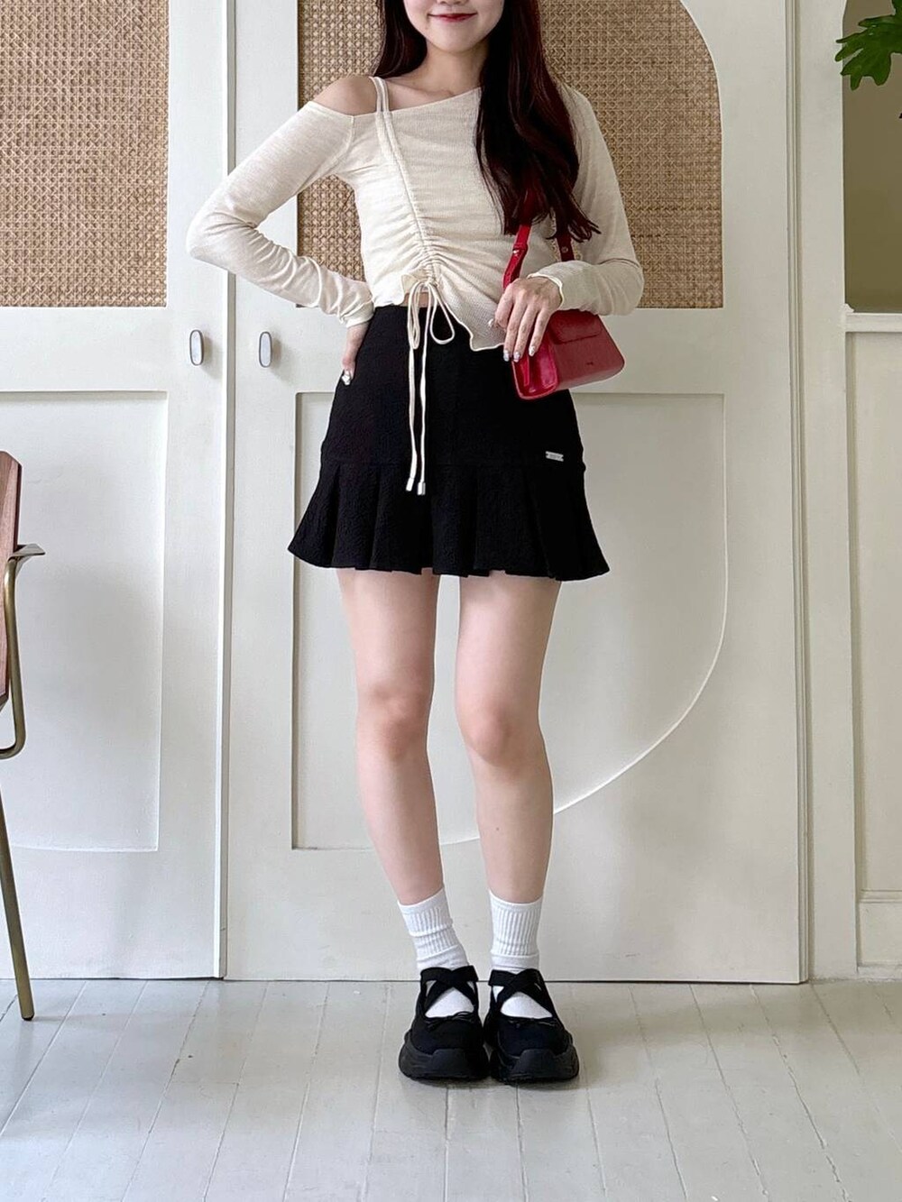 レッド系のショルダーバッグ、ベージュ系のTシャツ/カットソー、ブラック系のスカートを着用したレディースの秋コーディネートの2枚目の写真