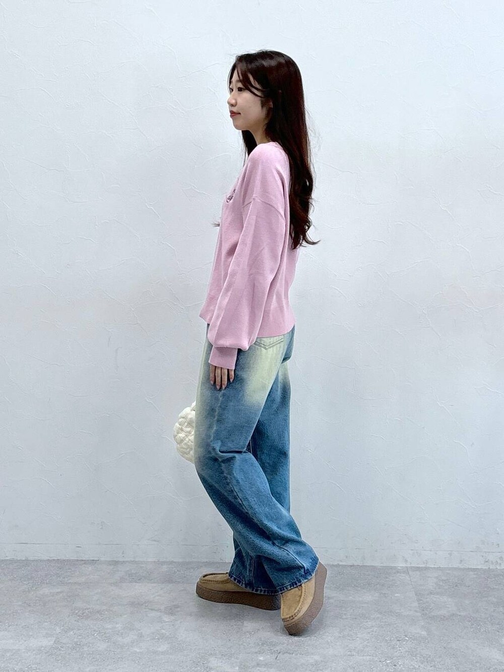 ホワイト系のショルダーバッグ、ピンク系のニット/セーター、ブルー系のデニムパンツを着用したレディースの秋コーディネートの3枚目の写真