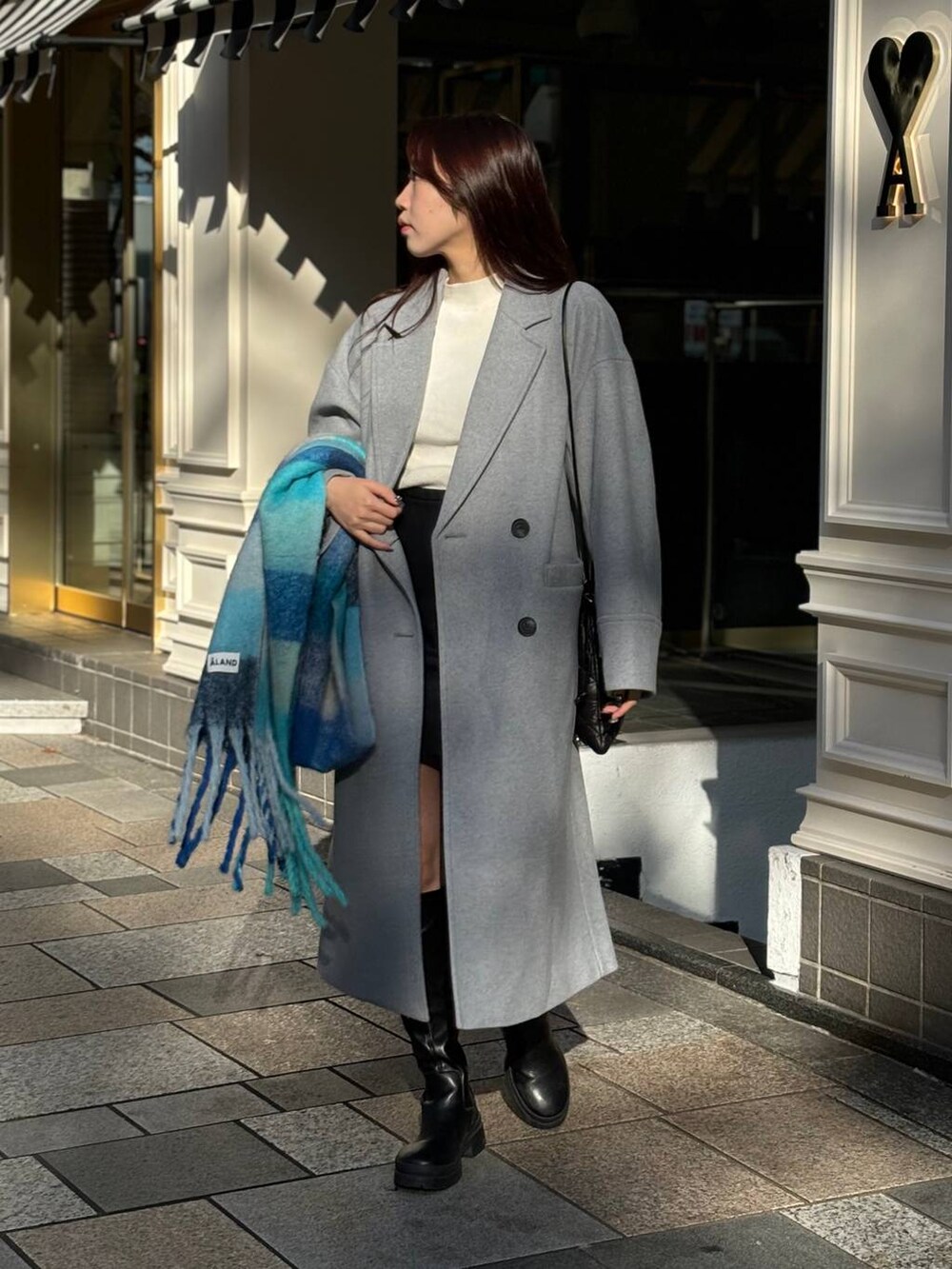グレー系のチェスターコート、ブラック系のショルダーバッグ、ブルー系のマフラーを着用したレディースの冬コーディネートの3枚目の写真