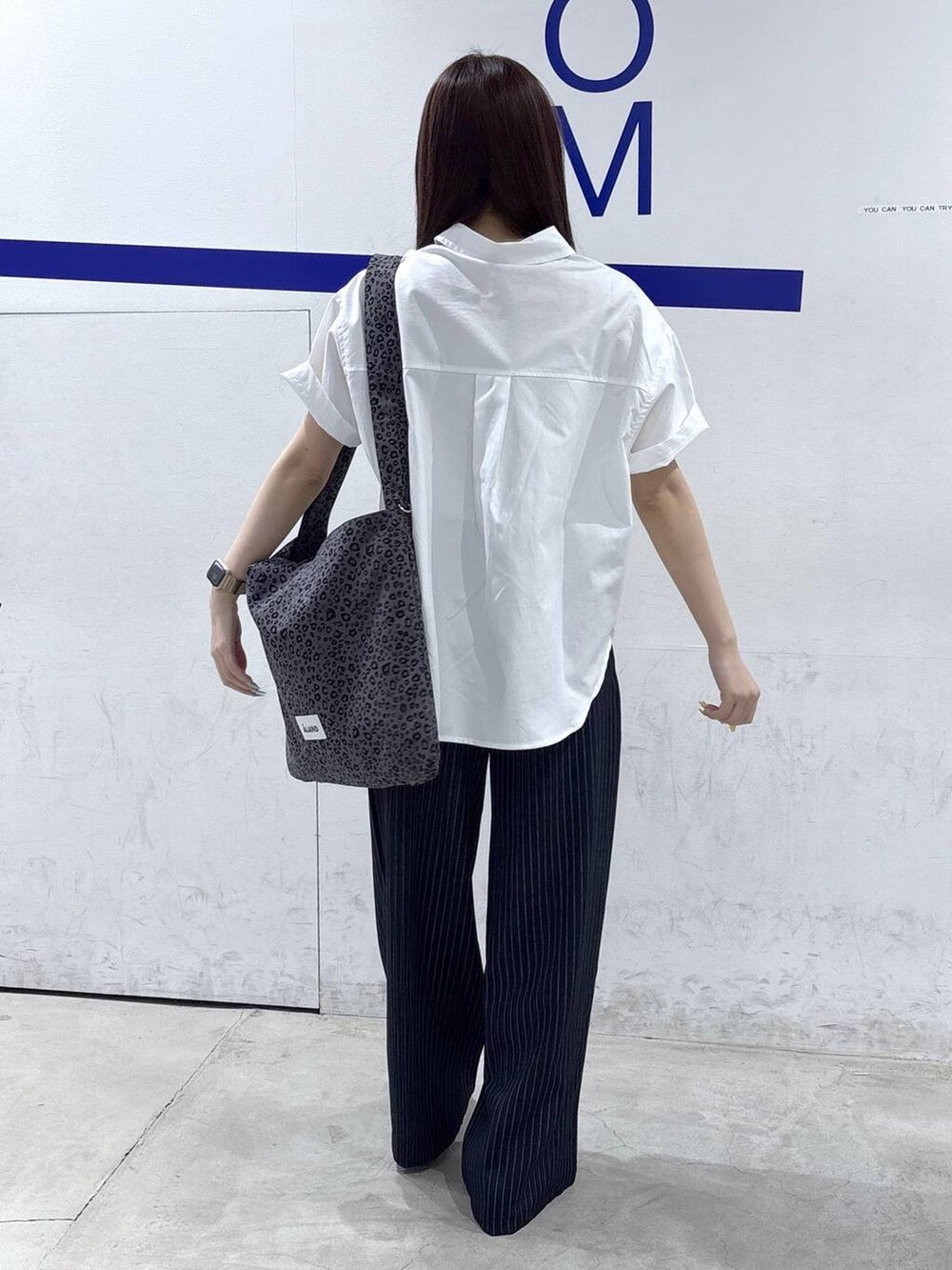 グレー系のトートバッグ、ブラック系のパンプス、ブルー系のスラックスを着用したレディースの春コーディネートの4枚目の写真
