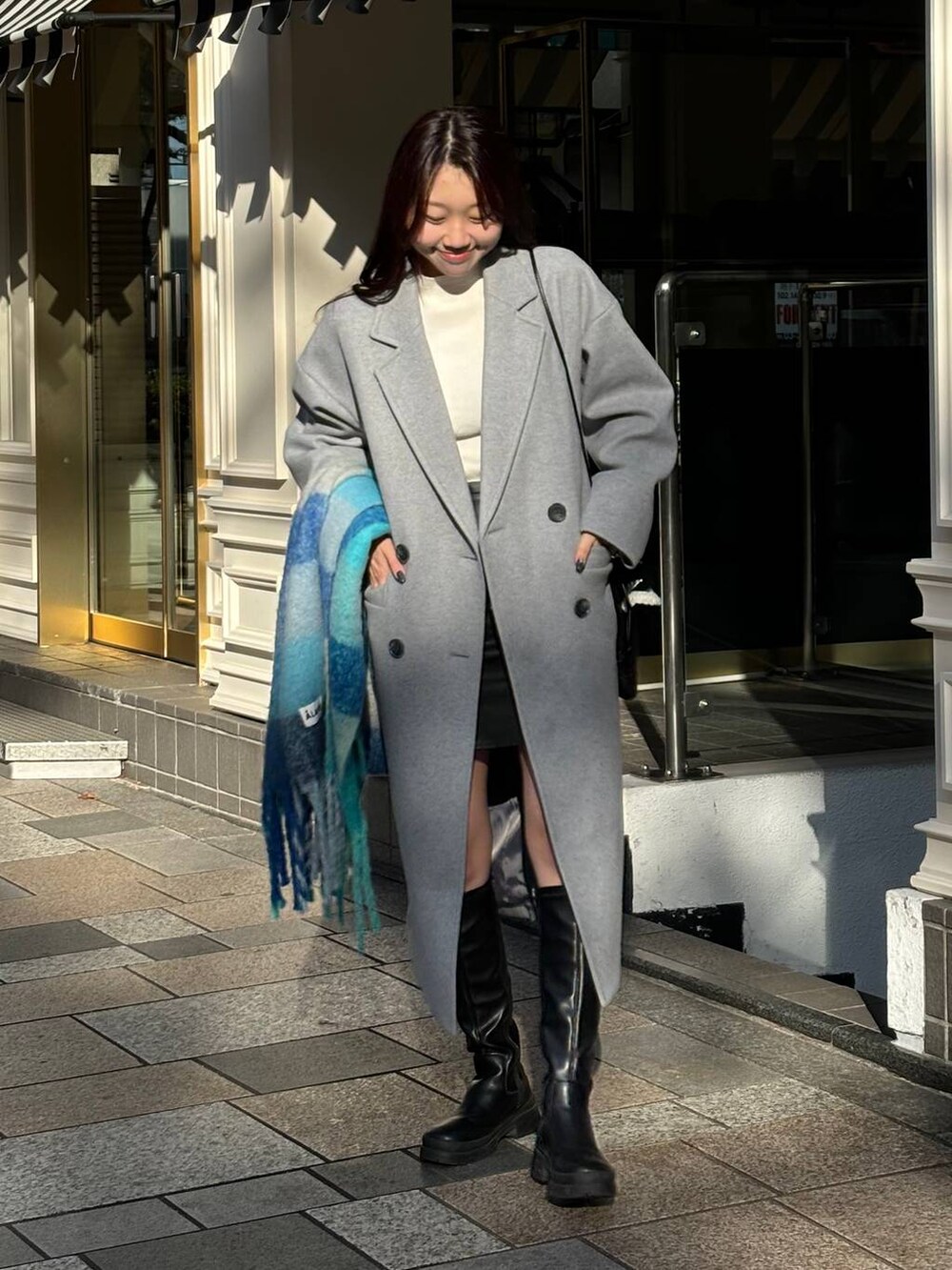 グレー系のチェスターコート、ブラック系のショルダーバッグ、ブルー系のマフラーを着用したレディースの冬コーディネートの4枚目の写真